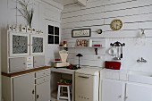 Retro dresser next to kitchen counter in corner of white, wood-clad kitchen