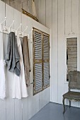 Towels hanging on row of coat hooks next to fitted wardrobe with rustic louvre doors in white wood-clad partition