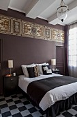 Double bed in bedroom with chequered floor and Art-Nouveau frieze on purple-painted wall