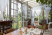 Antique furniture, floral crockery on dining table and wicker chairs in seating area in vintage-style conservatory