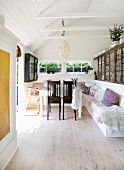 Dark wooden chairs at table and white-painted masonry bench in simple summer house