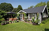 Kleines Sommerhaus schwarz gestrichen mit weissen Sprossenfenstern in sonnenbeschienenem Garten