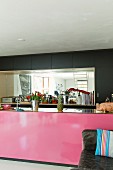 Pink kitchen island in front of black fitted cupboards with mirrored niche