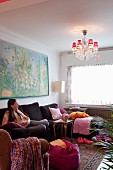 Woman sitting on couch in living room with comfortable furniture and chandelier with small red lampshades