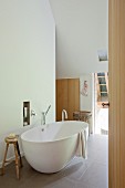 Freistehende weiße Badewanne auf grossformatigem Fliesenboden in modernem Bad im Dachgeschoss