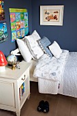 Bett mit Kissenstapel in dunkelblauer Kinderzimmerecke mit aufgehängten Postern