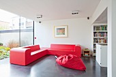 Red, foam, designer corner sofa and red beanbag on concrete floor in modern interior