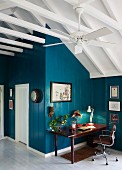 Desk in corner of room with wood panelling painted petrol blue and exposed pavilion roof