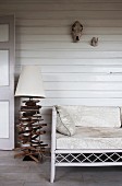 Maritime-style lamp base made of crossed pieces of driftwood next to ornate bamboo bench on white wooden veranda