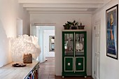 Fluffy lampshade on maritime sideboard and glass-fronted crockery cabinet painted green and silver in hallway