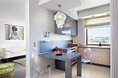 Victoria Ghost Stühle an integriertem Esstisch in der offenen Einbauküche; seitlich Blick in den Wohnraum mit Schwarz-Weiß-Portrait