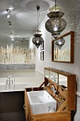 Oriental pendant lamps above custom-made washstand with lid; mirrored wall and pattern of grasses above bathtub in background