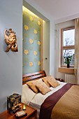 Niche with floral pattern and indirect lighting behind French bed; wooden sculpture on wall