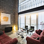 Sofa set with brocade pattern and fifties-style armchairs around ornate coffee table in modern interior with flatscreen TV and floor lamp against concrete-block wall