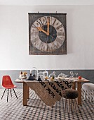 Eclectic interior with tiled floor, table set with glassware, Eames chair and old church tower clock on wall