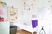 White cot below garland and vintage botanical illustration on wall of nursery