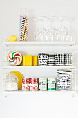 Black and white beakers and bowls, tinned food, glasses and drinking straws on white, wall-mounted shelves
