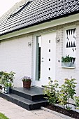 Wohnhaus mit geweisselter Ziegelfassade, vor weisser Haustür schwarze Podeststufen, seitlich schmale Beete