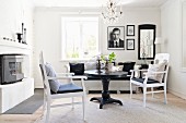Schwarzer, runder Tisch und weiße Armlehnstühle in gemütlicher Wohnzimmerecke