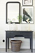 Black-painted console table, seagrass basket and pictures on wood-clad wall