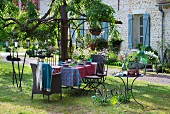 Gedeckter Gartentisch mit Stühlen aus Rattan und Metall, nostalgische Windlichter und Kerzenhalter