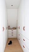Black ladies' shoes on wooden floor of narrow dressing room with white fitted wardrobes