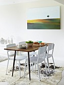 Simple dining table and white chairs on cowhide rug and modern landscape painting on wall