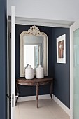 View through open double doors of console table and white wood-framed mirror on dark blue hall wall
