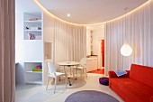 Orangerotes Sofa und weiße Ghost Stühle mit Tisch in kreisförmigem Wohnbereich, Vorhang als Raumteiler in modernem Ambiente