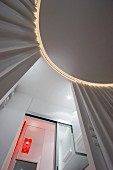 View from below of circular ceiling panel with indirect lighting and curtains; orange lamp in bathroom seen through open sliding door