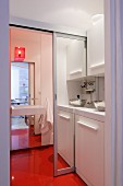 Kitchenette with open mirrored sliding door leading to bathroom with continuous orange floor