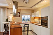 Designer kitchen with white cabinets, wooden worksurface, stainless steel extractor hood and recessed spotlights integrated in ceiling frieze