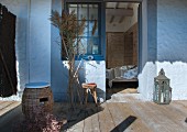 Wicker stool with seat cushions and bunch of pampas grass on wooden terrace with view into bedroom