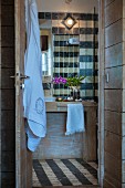 Towel hanging on open door and washstand against tiled wall in rustic bathroom