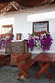 Tische und Gartenbänke vor Bauernhaus mit blühenden Blumenkästen und Deko mit geerntetem Graumohn