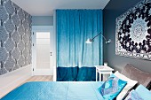 Rug on wall above double bed with pale blue covers, two-tone blue curtain screening wardrobe in niche