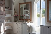 Elegant, rustic bathroom; custom washstand with white base cabinets, fitted shelving in niche, arched window and window seat