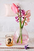 Hyacinths and tulips in pink glass vase next to tealight holder printed with retro-style photo on wooden surface