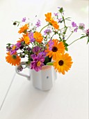 Vase of marigolds and purple flowers in white china jug