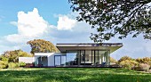 Classic modern house with projecting roof and glass facade on hill in open, summery landscape