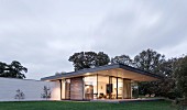 Abendstimmung über modernem Wohnhaus mit auskragendem Dach über Terrasse, beleuchteter transparenter Innenraum