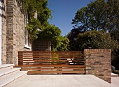 Stone terrace with bench integrated in fence adjoining old house with brick facade