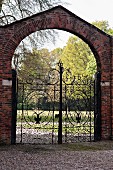 Ornate wrought iron gate in brick wall with rounded arch leading to park