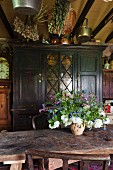 Vase of flowers on rustic wooden table in front of vintage cupboard with glass door panels in country-house kitchen