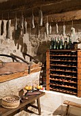 Wine rack and home-made salami hanging from wooden beams in rustic pantry