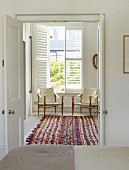 Open double doors with view of colourful rug and delicate armchairs with ecru covers below window