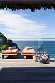 Sun loungers with orange cushions on wooden terrace with glass balustrade and sea view