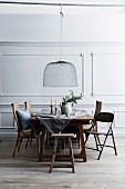 Rustic wooden table with various chairs, above pendant lamp with wire mesh shade