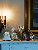 Snow globes with festive motifs in front of gilt-framed mirror on mantelpiece