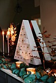 Triangular, fir-tree-shaped chest of tiny drawers as perpetual Advent calendar arranged on mantelpiece with plants and candles